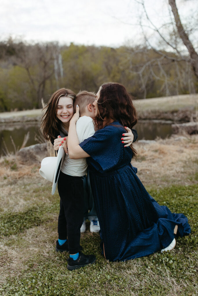 mother in a blue dress hugging her son while older daughter is also leaning in for a hug, family hugging