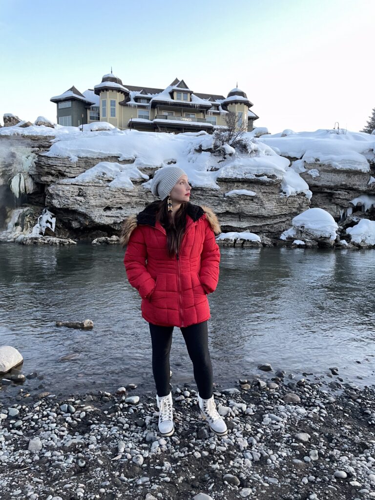 gorgeous brunette woman in a red coat standing in front of a frozen river.