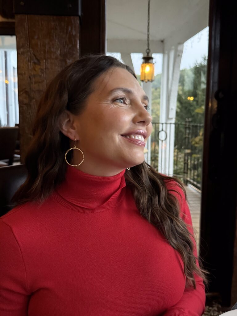Beautiful, brunette woman in a red dress, smiling softly while looking out the window.